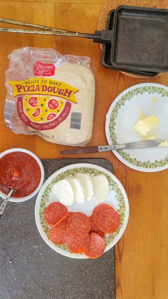 ingredients to make pie iron pizzas with pizza dough, pizza sauce, mozzarella, butter and toppins