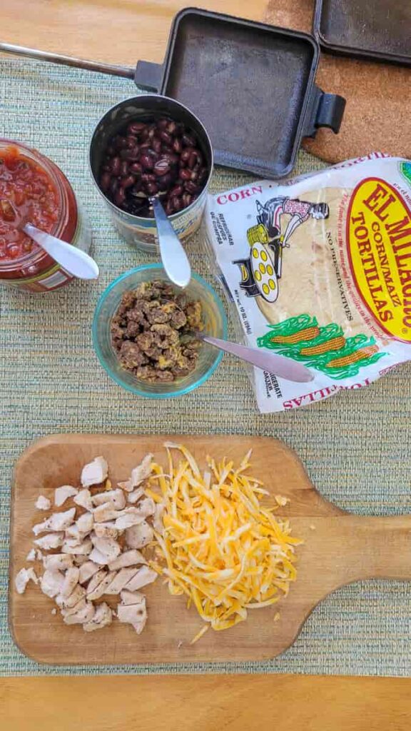 campfire taco ingredients with corn tortillas, taco meat, cheese, beans and salsa