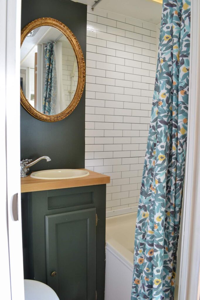 rv bathroom remodel with green cabinets, subway tile, floral shower curtain and wood accent wall for storage