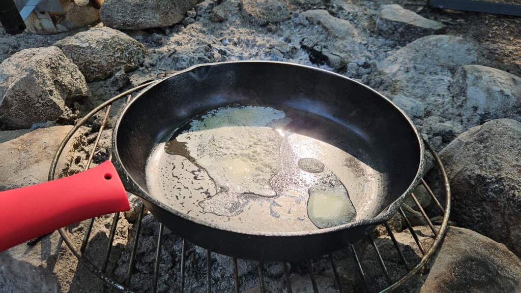 cast iron skillet cooking over the campfire in egg breakfast recipe