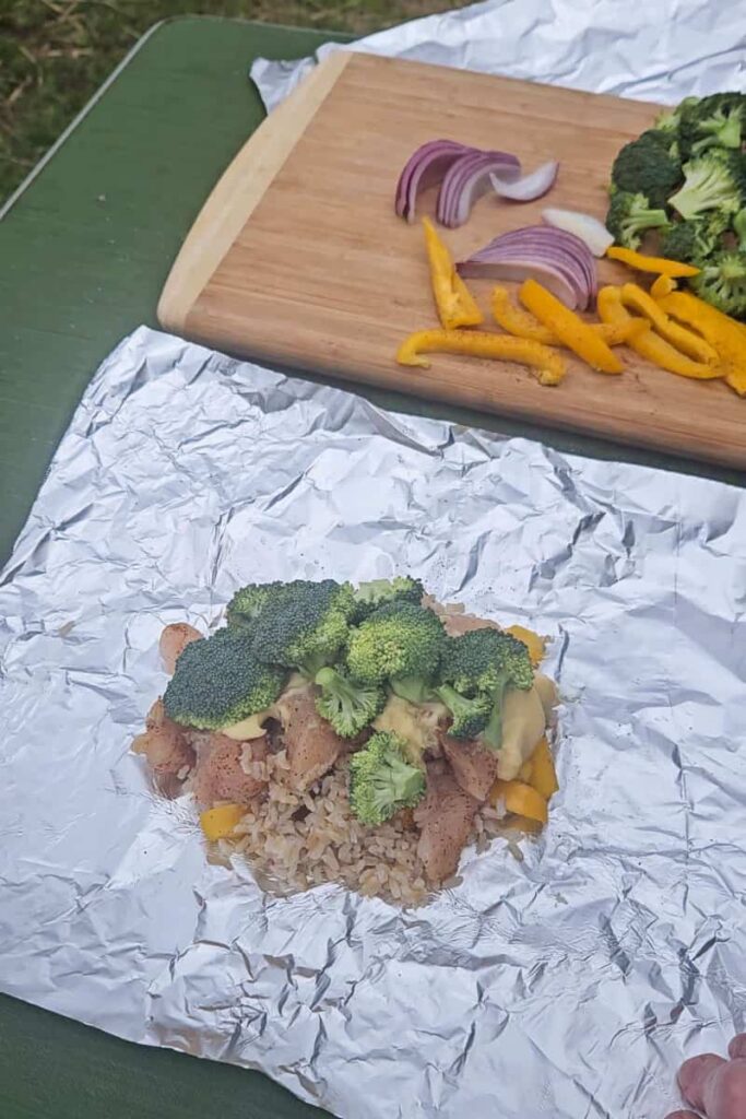 camping foil packet dinner with chicken, broccoli and rice cooked over campfire