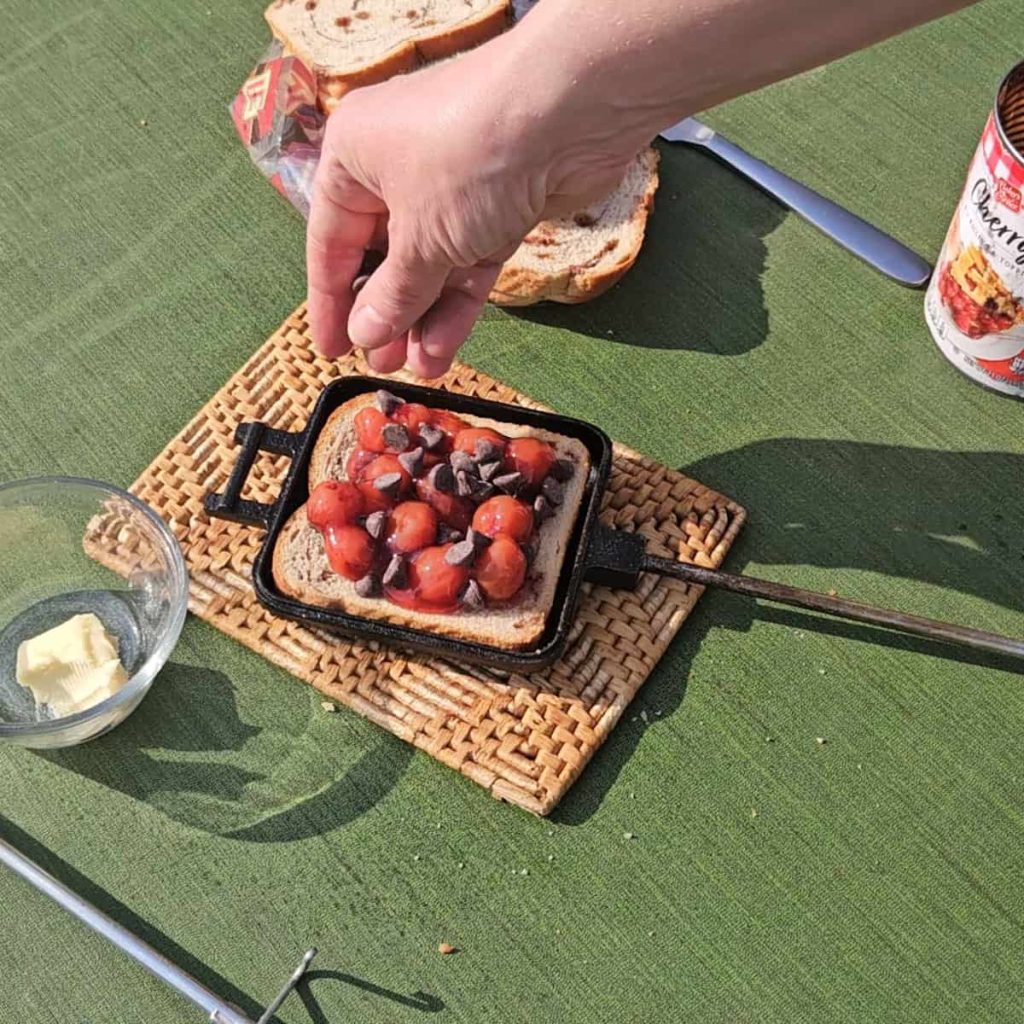 steps to make campfire hobo pie dessert with chocolate and cherries over the campfire in a pie iron