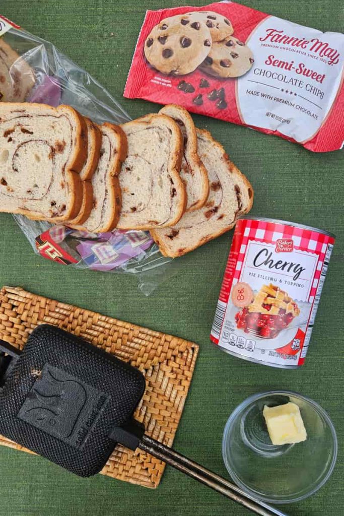 easy ingredients to make camping hobo pie dessert in a pie iron with canned cherries, bread, and chocolate chips
